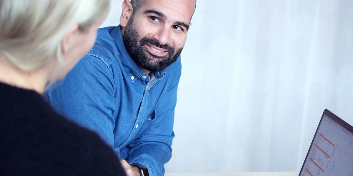 En man som sitter vid datorn och lyssnar på sin kollega som sitter bredvid